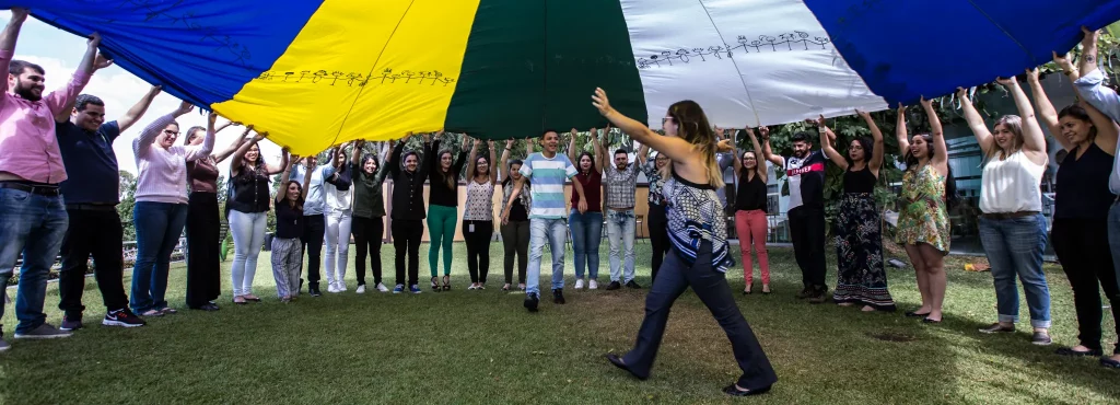 Pessoas segurando uma lona em uma dinâmica em grupo realizada no jardim da Cosy Casa Mirante